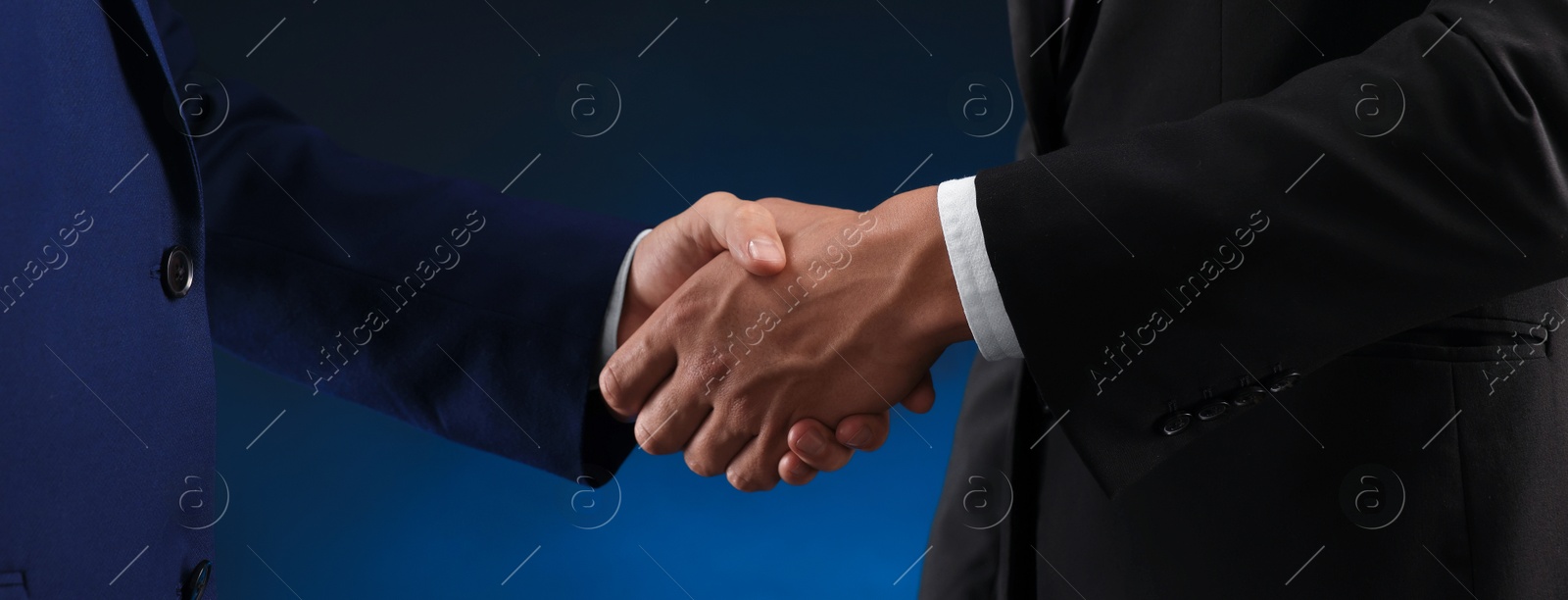 Photo of Business partners shaking hands on dark blue background, closeup