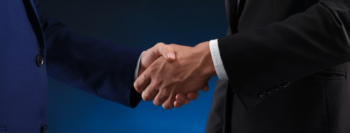 Photo of Business partners shaking hands on dark blue background, closeup