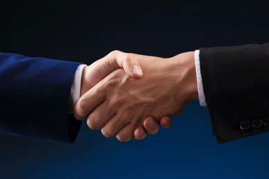 Photo of Business partners shaking hands on dark blue background, closeup
