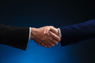 Photo of Business partners shaking hands on dark blue background, closeup