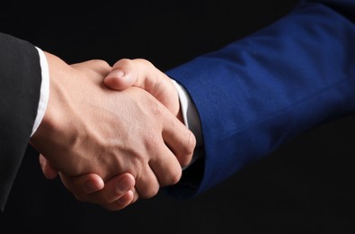 Photo of Business partners shaking hands on black background, closeup