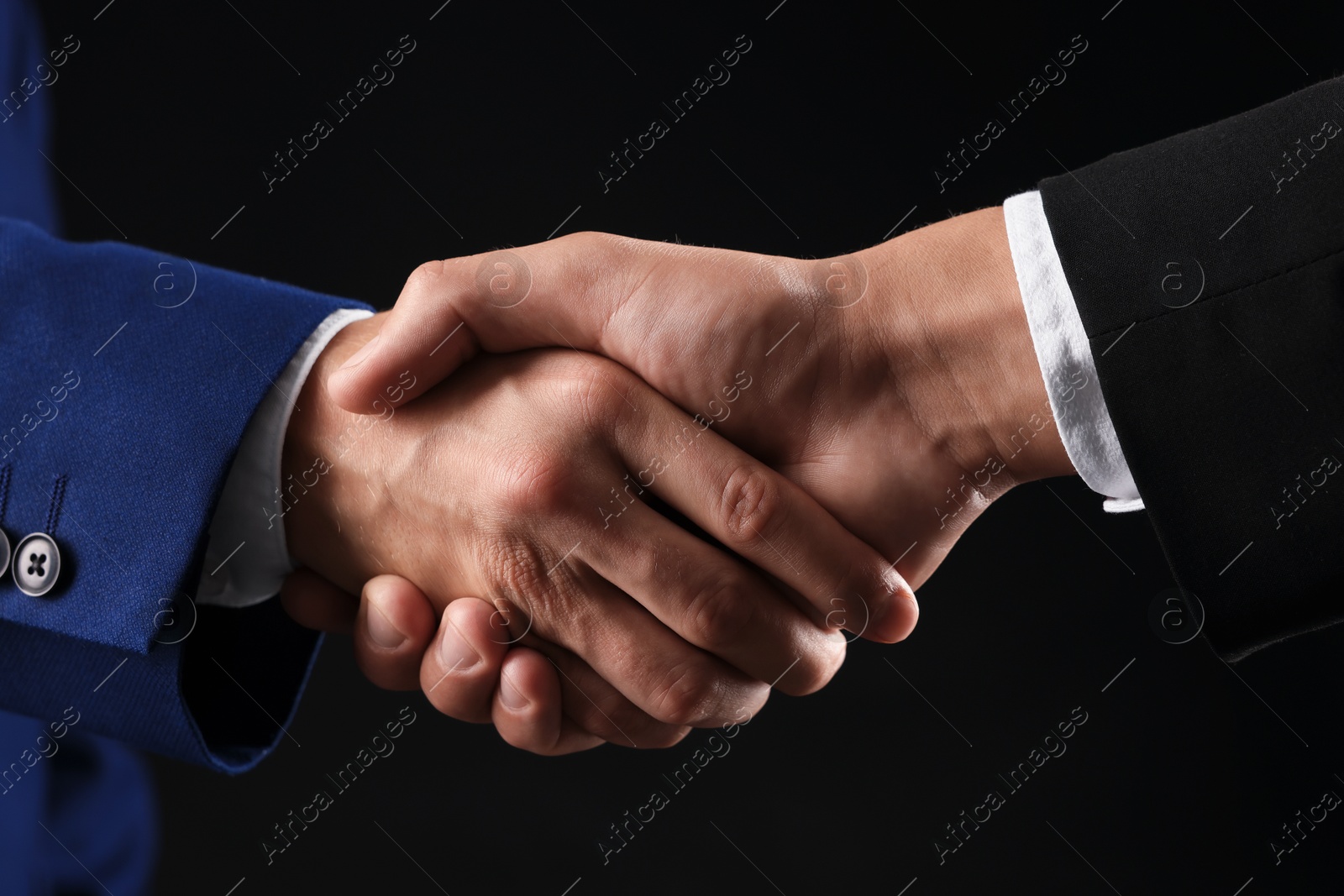 Business partners shaking hands on black background, closeup Photo of Business partners shaking hands on black background, closeup