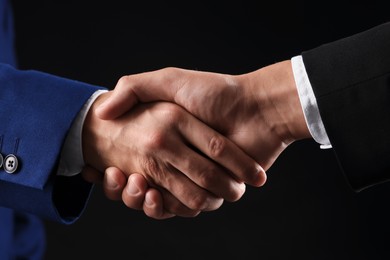 Photo of Business partners shaking hands on black background, closeup