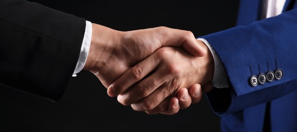 Photo of Business partners shaking hands on black background, closeup