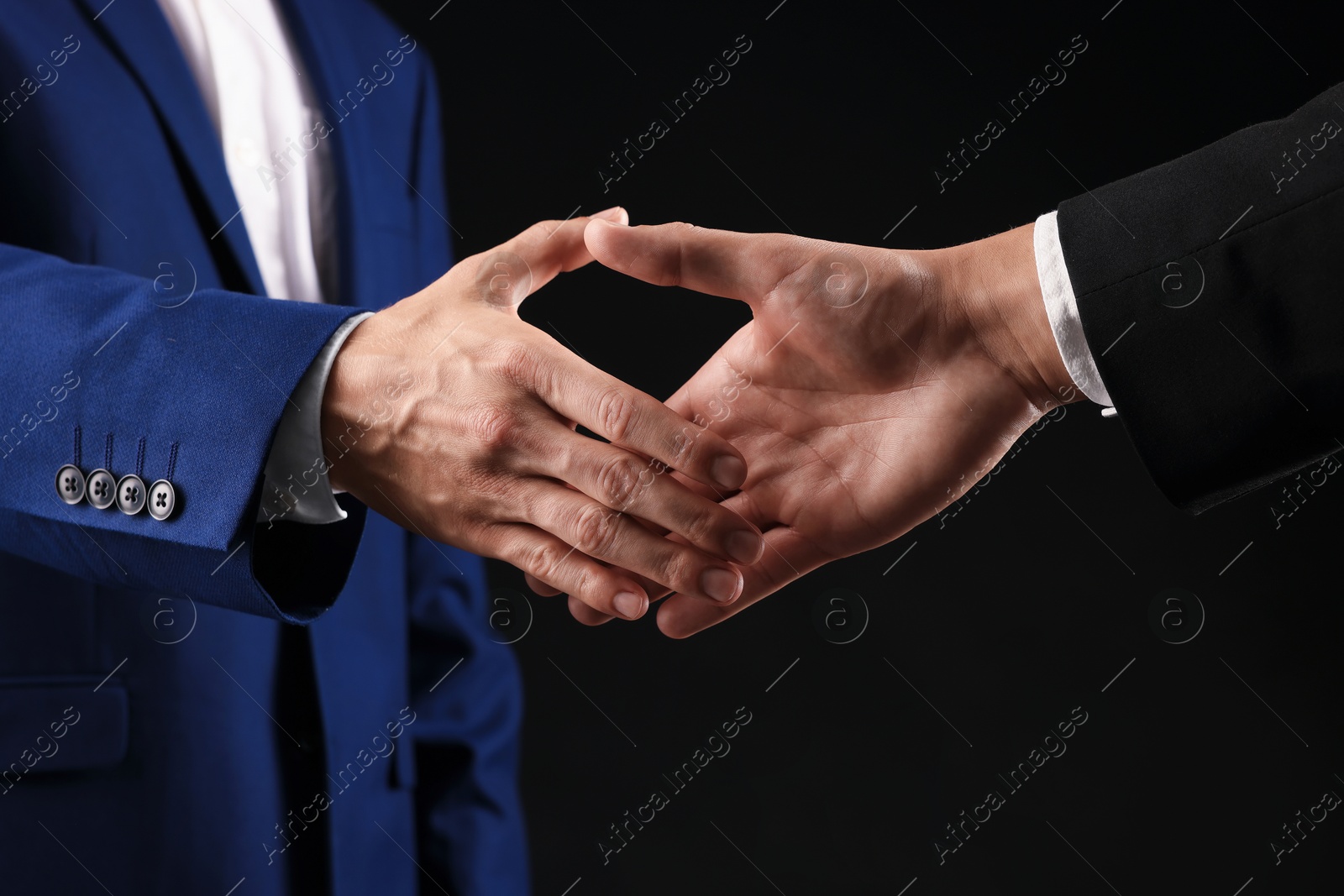 Business partners shaking hands on black background, closeup Photo of Business partners shaking hands on black background, closeup