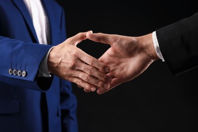 Photo of Business partners shaking hands on black background, closeup
