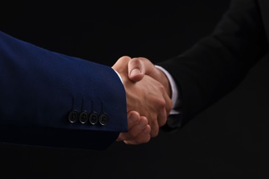 Photo of Business partners shaking hands on black background, closeup