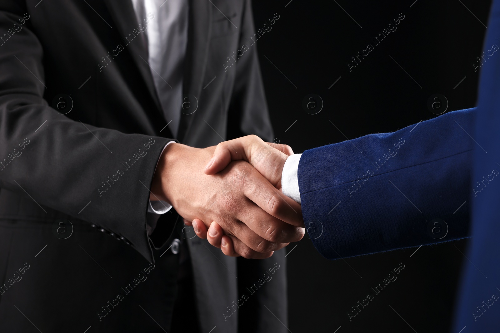 Business partners shaking hands on black background, closeup Photo of Business partners shaking hands on black background, closeup