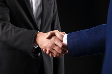 Photo of Business partners shaking hands on black background, closeup