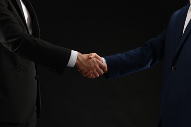 Photo of Business partners shaking hands on black background, closeup