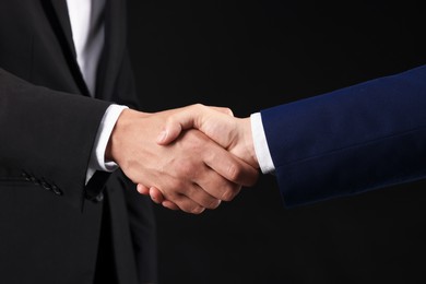 Photo of Business partners shaking hands on black background, closeup