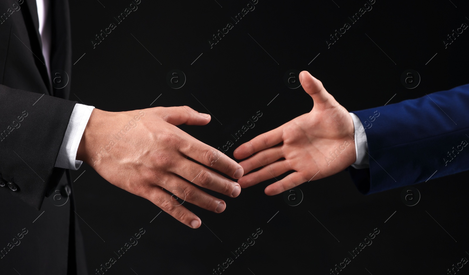 Business partners shaking hands on black background, closeup Photo of Business partners shaking hands on black background, closeup