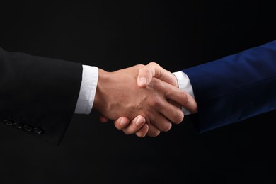 Photo of Business partners shaking hands on black background, closeup