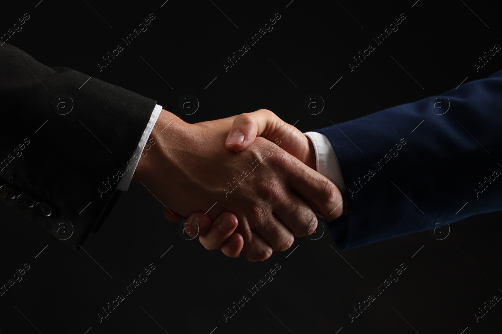 Business partners shaking hands on black background, closeup Photo of Business partners shaking hands on black background, closeup