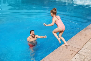 Photo of Father and his daughter having fun in swimming pool outdoors. Family vacation