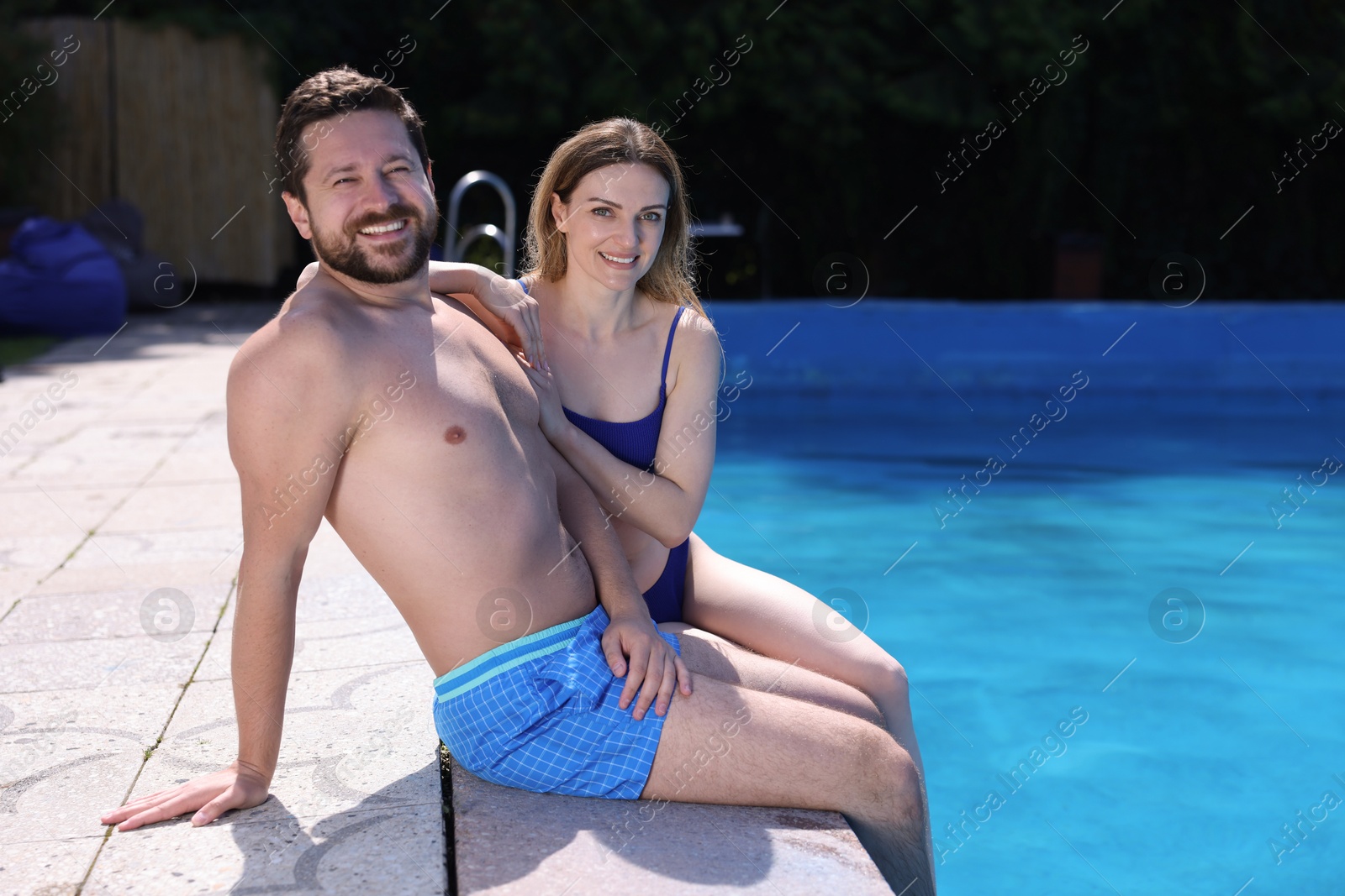 Happy couple at poolside outdoors on sunny day, space for text. Family vacation Photo of Happy couple at poolside outdoors on sunny day, space for text. Family vacation