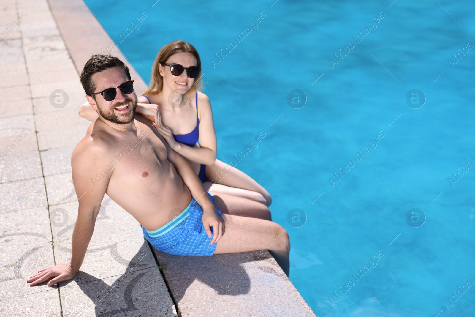 Happy couple at poolside outdoors on sunny day, space for text. Family vacation Photo of Happy couple at poolside outdoors on sunny day, space for text. Family vacation