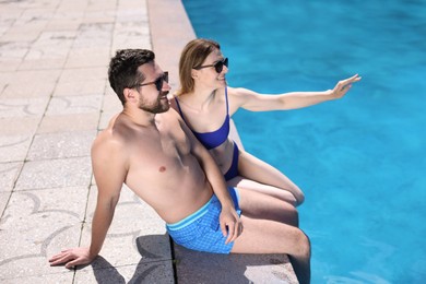 Photo of Happy couple at poolside outdoors on sunny day. Family vacation