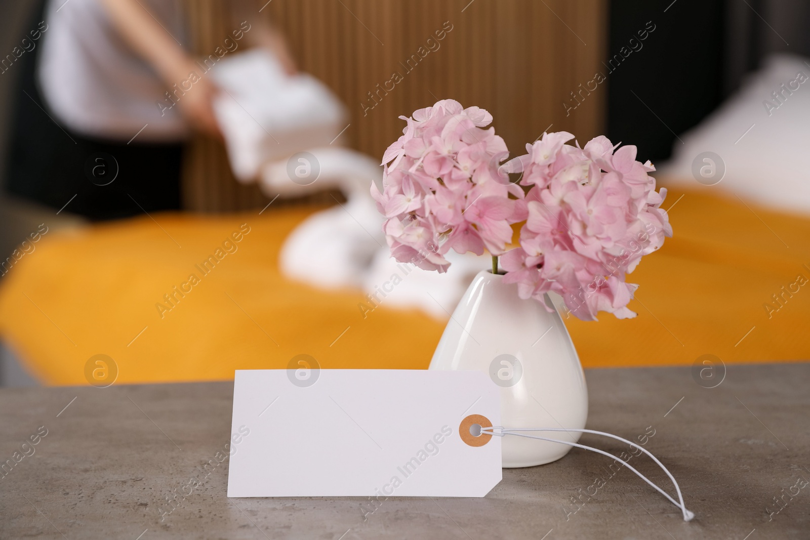 Welcome. Chambermaid making bed in hotel room, focus on blank card and hydrangea flowers Photo of Welcome. Chambermaid making bed in hotel room, focus on blank card and hydrangea flowers