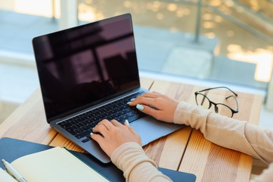 Photo of Teenage girl using laptop at wooden desk indoors, closeup. Home workplace