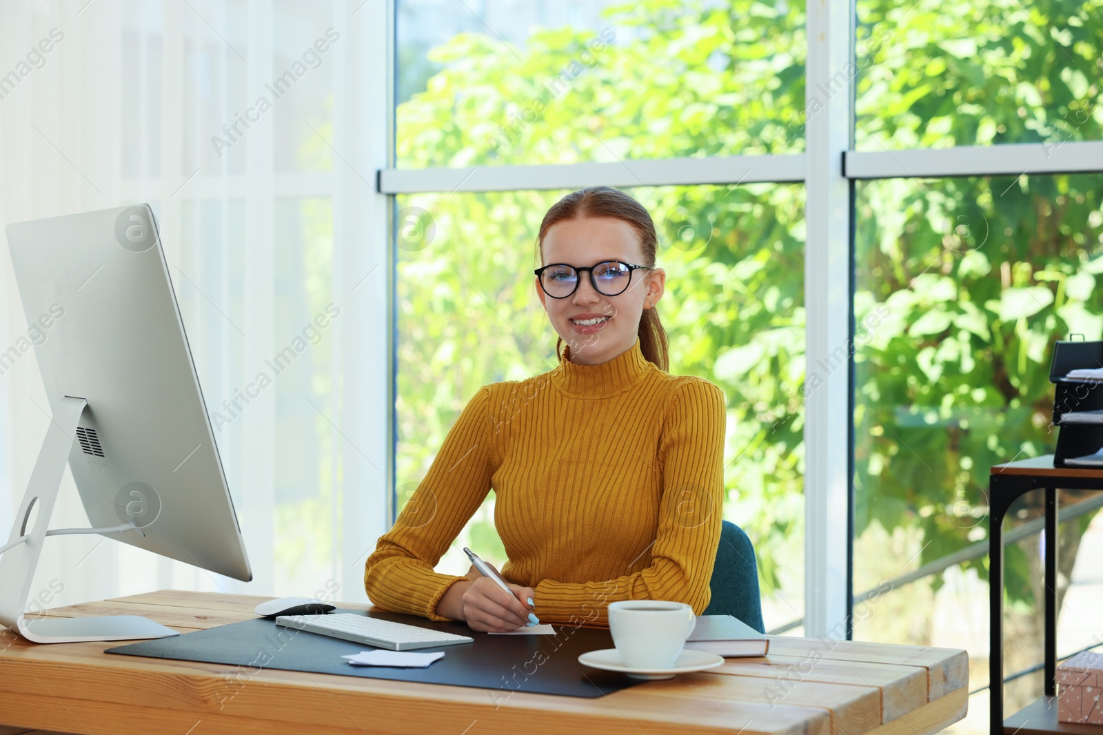 Teenage girl using computer and writing in notebook at wooden desk indoors. Home workplace Photo of Teenage girl using computer and writing in notebook at wooden desk indoors. Home workplace