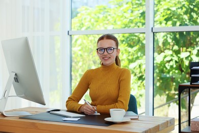 Photo of Teenage girl using computer and writing in notebook at wooden desk indoors. Home workplace