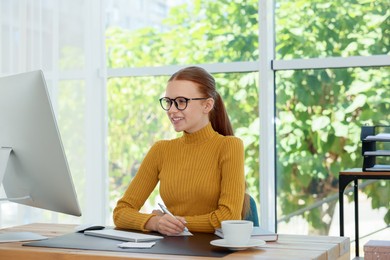 Photo of Teenage girl using computer and writing in notebook at wooden desk indoors. Home workplace