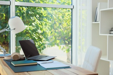 Photo of Home workplace. Laptop, headphones, coffee and stationery on wooden table, space for text
