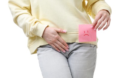 Photo of Woman holding sticky note with drawn sad face and suffering from cystitis symptoms on white background, closeup