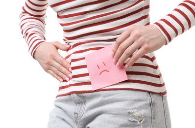 Photo of Woman holding sticky note with drawn sad face and suffering from cystitis symptoms on white background, closeup