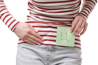 Photo of Woman holding sticky note with drawn sad face and suffering from cystitis symptoms on white background, closeup