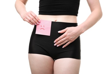 Photo of Woman holding sticky note with drawn sad face and suffering from cystitis symptoms on white background, closeup
