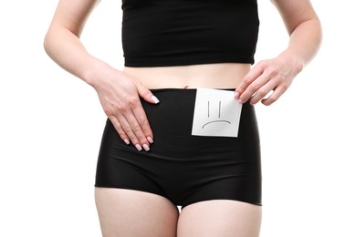 Photo of Woman holding sticky note with drawn sad face and suffering from cystitis symptoms on white background, closeup