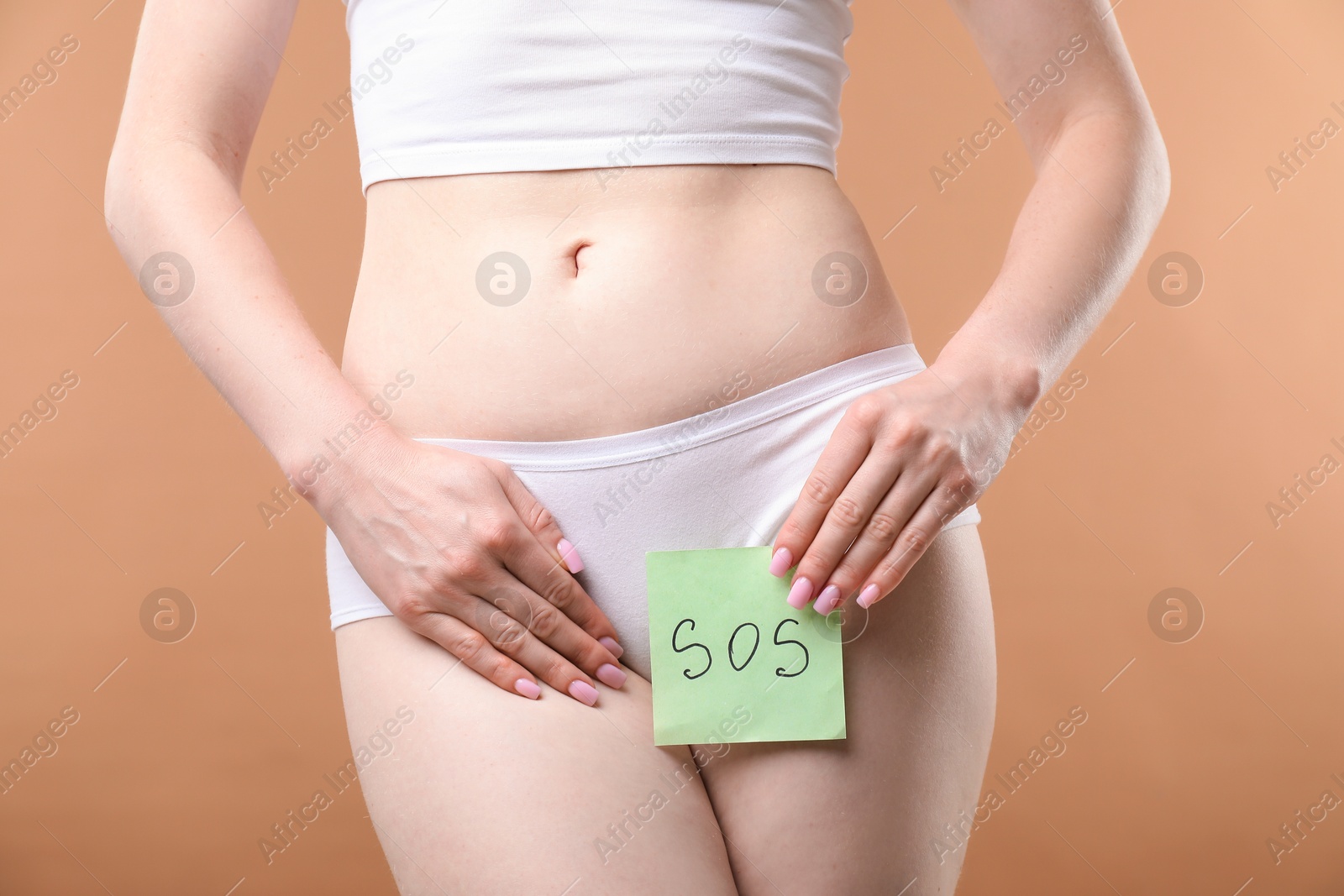 Photo of Woman holding sticky note with word SOS and suffering from cystitis symptoms on dark beige background, closeup
