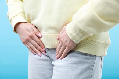 Photo of Woman suffering from cystitis symptoms on light blue background, closeup