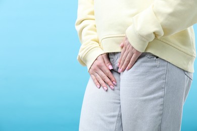 Photo of Woman suffering from cystitis symptoms on light blue background, closeup. Space for text