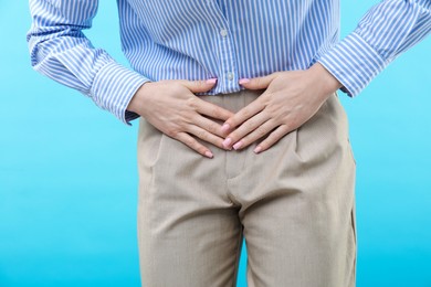 Photo of Woman suffering from cystitis symptoms on light blue background, closeup