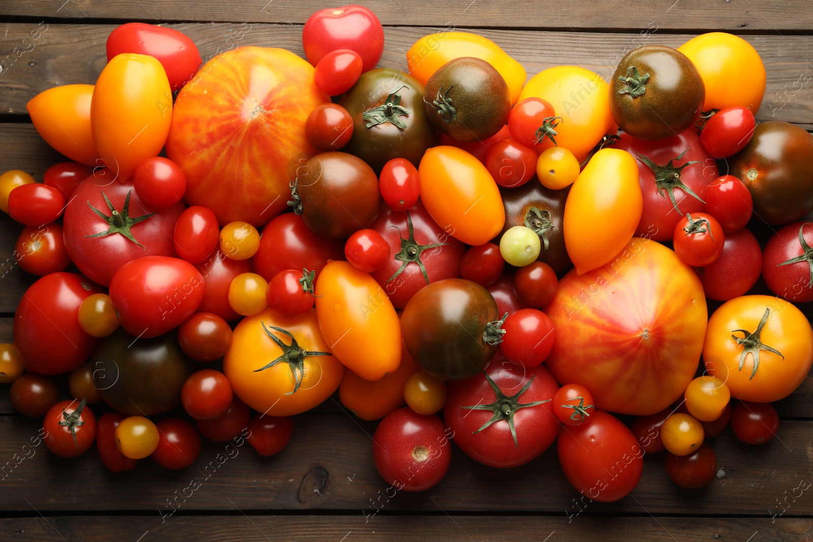 Photo of Many different ripe tomatoes on wooden table, flat lay