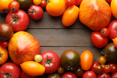 Photo of Frame of many different ripe tomatoes on wooden table, flat lay. Space for text