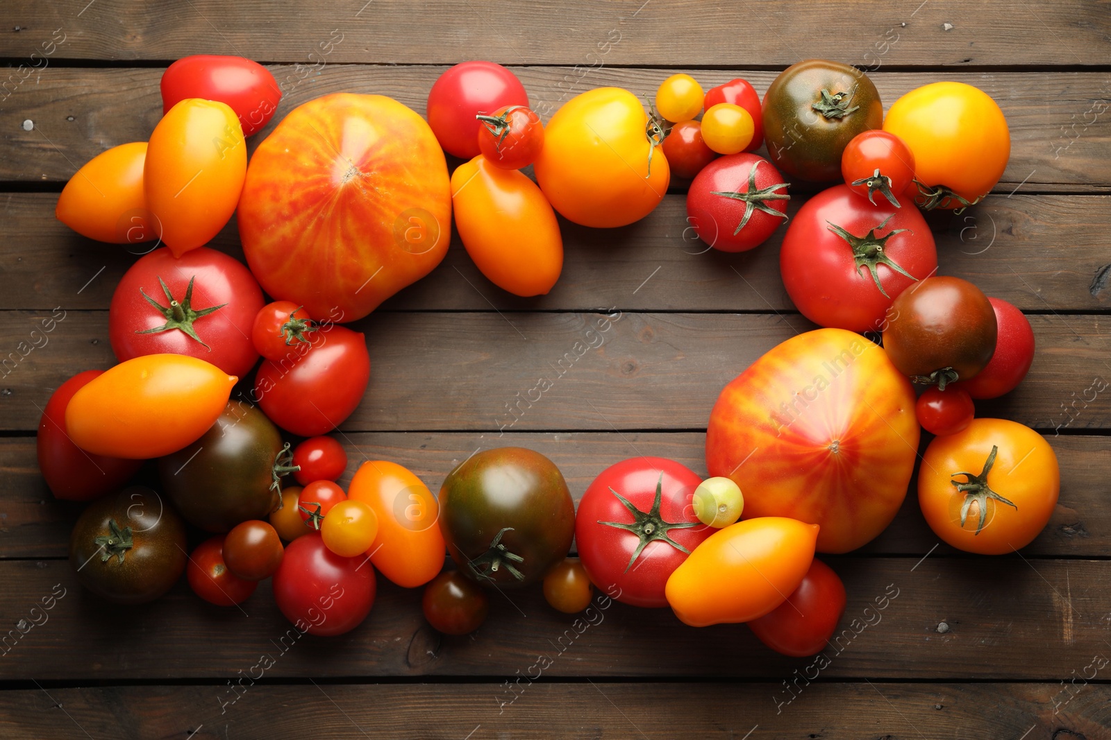 Photo of Frame of many different ripe tomatoes on wooden table, flat lay. Space for text