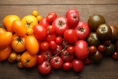 Photo of Many different ripe tomatoes on wooden table, flat lay