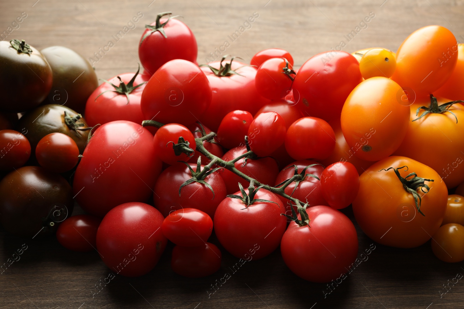 Photo of Many different ripe tomatoes on wooden table, closeup