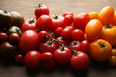 Photo of Many different ripe tomatoes on wooden table, closeup