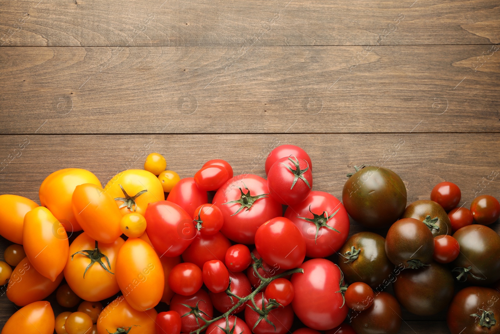 Photo of Many different ripe tomatoes on wooden table, flat lay. Space for text