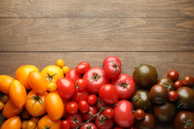 Photo of Many different ripe tomatoes on wooden table, flat lay. Space for text