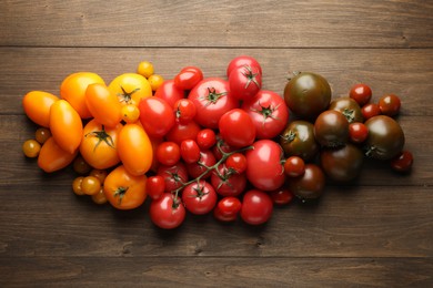 Photo of Many different ripe tomatoes on wooden table, flat lay