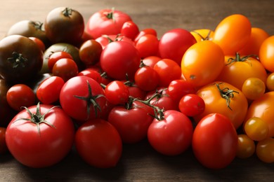 Photo of Many different ripe tomatoes on wooden table, closeup