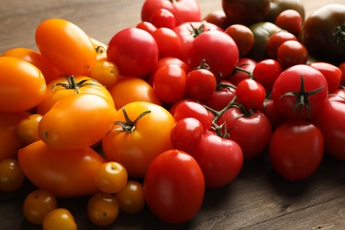 Photo of Many different ripe tomatoes on wooden table, closeup