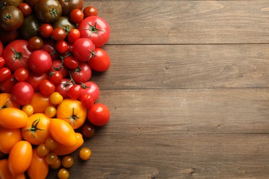 Photo of Many different ripe tomatoes on wooden table, flat lay. Space for text