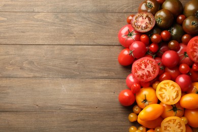 Photo of Many different ripe tomatoes on wooden table, flat lay. Space for text
